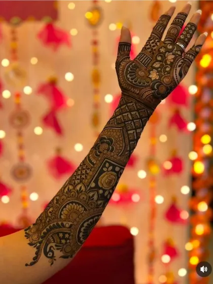 A side view of a full-arm mehandi, showing how the pattern wraps completely around the arm. The festive lights in the background add to the celebratory feel.