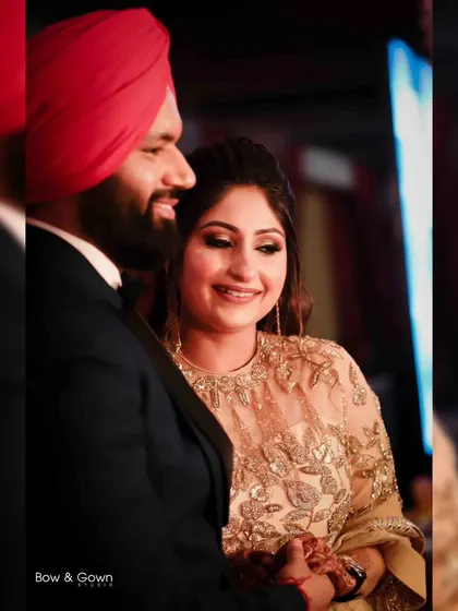 A candid moment of a Sikh couple sharing a smile during their engagement celebration. The warm lighting and their genuine happiness make this a beautiful, intimate shot.