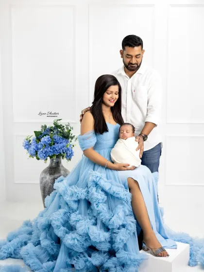A beautiful family portrait featuring a mother in a stunning blue gown, holding her newborn alongside her partner. This showcases a more formal, elegant style of family photography.