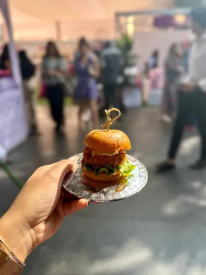 A hand holding a mini slider, part of the delicious spread at the Luxe Shopping Experience pop-up event.