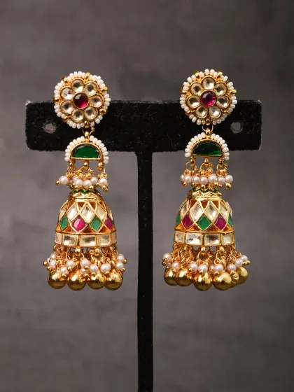 A vibrant pair of meenakari jhumkas. The bell is enameled with red, green, and white, while the pearl-studded floral top adds a classic touch to this colorful design.