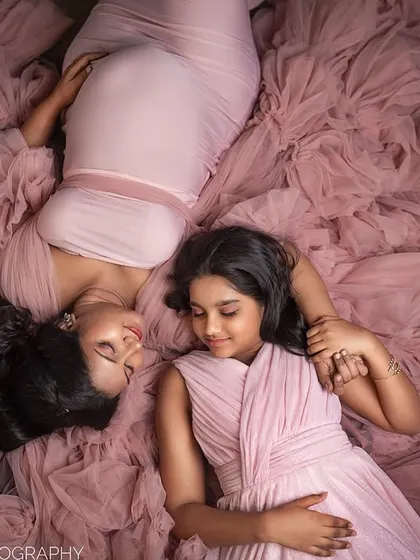 An aerial shot of a mother-to-be and her daughter lying peacefully on a sea of pink fabric. This artistic composition is both visually stunning and emotionally tender.