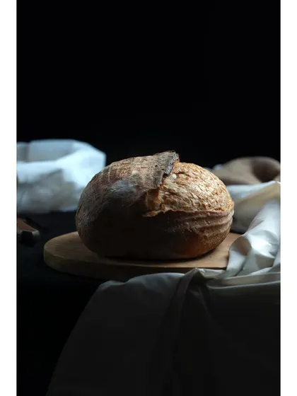 A rustic loaf of sourdough bread, shot in a classic chiaroscuro lighting style. The play of light and shadow emphasizes the crust's texture, ideal for bakeries and artisanal food brands.