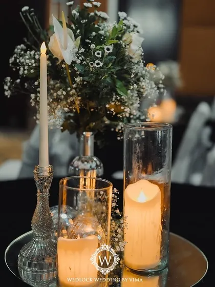 An elegant centerpiece for a Sangeet night, featuring white florals, baby's breath, and candles on a mirrored tray. The mini disco balls add a touch of sparkle and fun, tying into the party theme.