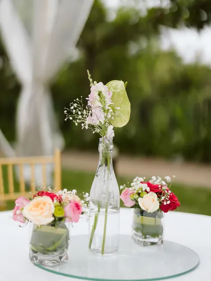 Simple, elegant centerpieces for guest tables. A small collection of glass bottles and vases with fresh roses and baby's breath adds a touch of beauty to every corner of the celebration.