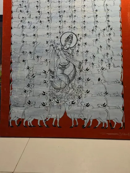 This painting of Lord Krishna surrounded by cows is a classic theme in Indian art. The monochromatic style with a bold red border gives it a contemporary feel while honoring a traditional subject.