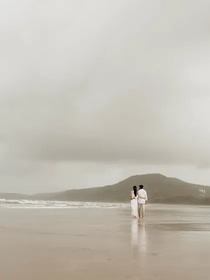 Walking towards the ocean together. This wide shot captures the couple against a dramatic, cloudy sky and rolling hills, symbolizing the start of their grand journey.