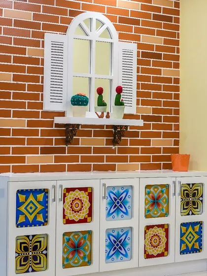 A vibrant and eclectic crockery cabinet with colorful, patterned glass doors. This piece adds a pop of personality and charm to the dining area, set against a rustic brick-finish wall.