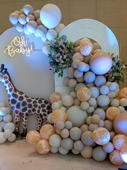 A wild and chic "Oh Baby" shower with a safari twist. A large giraffe prop stands next to a cascade of neutral-toned balloons with giraffe print accents.