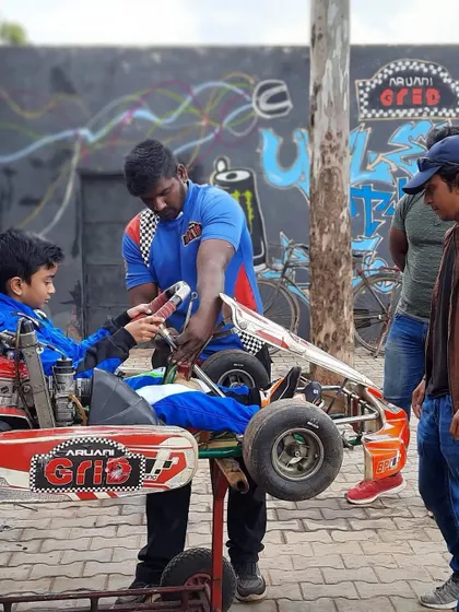 A young driver getting his kart adjusted by a mechanic.