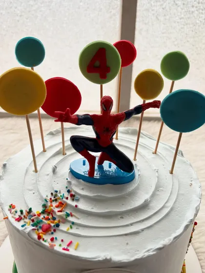 Spider-Man and cars, two favorites in one cake! This design features a Spidey topper, colorful cars around the base, and bright lollipop-style decorations.
