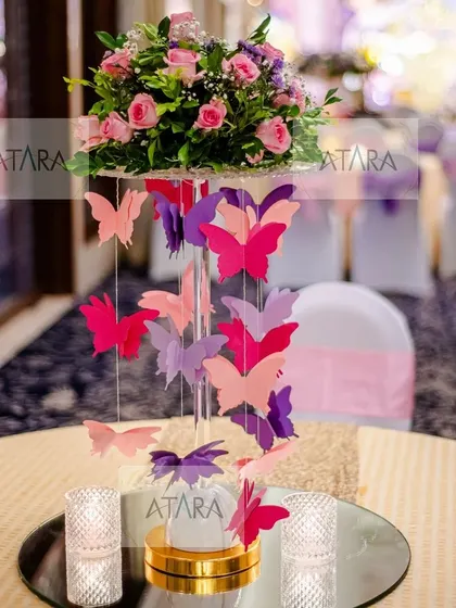 A beautiful and creative centerpiece for a butterfly-themed party. A cascade of colorful paper butterflies hangs from a floral arrangement, creating a dynamic and eye-catching table decoration.