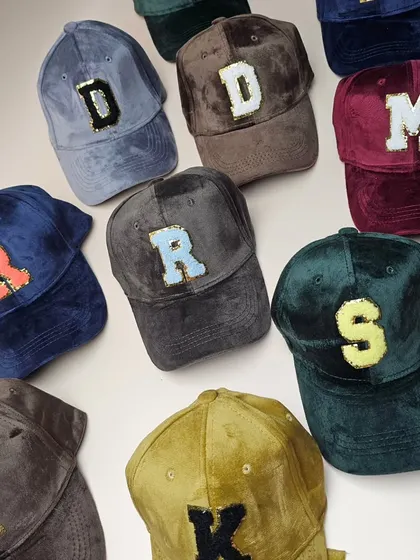 An overhead shot of our colorful collection of personalized suede caps, showing the different letter and color combinations available.