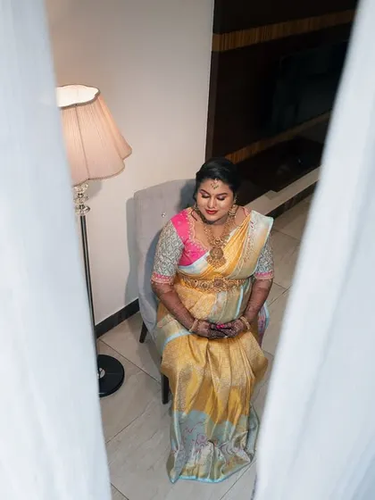 A high-angle shot taken through sheer curtains, creating a soft and intimate portrait of the expectant mother seated peacefully.