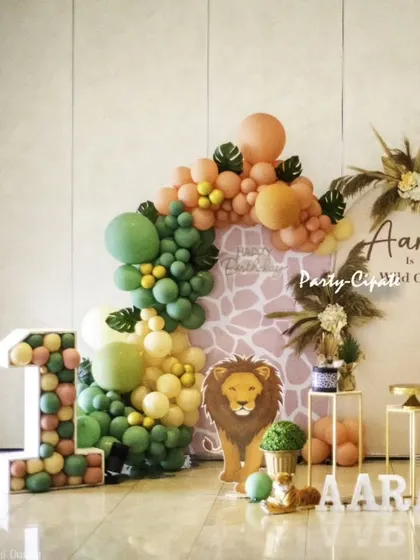 This setup for Aaran's party features a large light-up '1', a lion cutout, and a balloon arch in earthy tones. It's a modern and stylish way to celebrate a first birthday.
