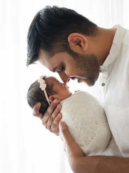 A father holds his swaddled newborn daughter, their noses touching in a sweet gesture. This is a classic and heartwarming father and newborn pose.