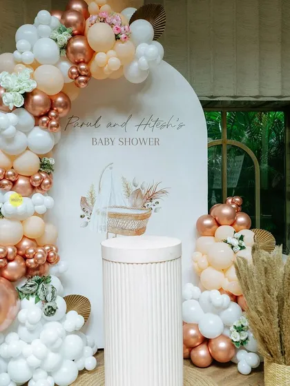 A beautiful boho-chic baby shower backdrop. The combination of a custom-printed arch, a pampas-adorned balloon garland in rose gold and white, and a simple plinth for the cake creates an effortlessly elegant look.