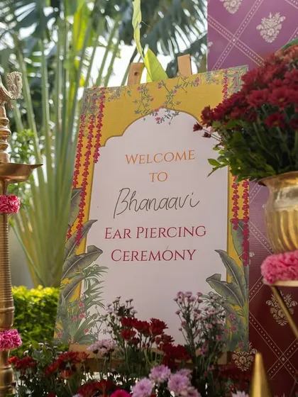 A close-up of the welcome sign and traditional brass lamp (diya) for Bhanu's ear piercing ceremony, capturing the fine details of the decor.