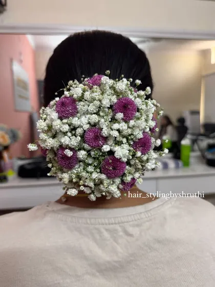 A full and rounded floral bun created using a mix of baby's breath and purple pom-pom flowers. This style adds a vibrant pop of color and is a great choice for sangeet or mehendi events.