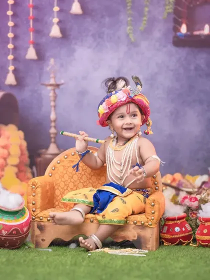 A happy little Krishna enjoying his time on the throne, holding his flute. This full setup includes hanging decorations, earthen pots, and soft grass for a complete Vrindavan feel.