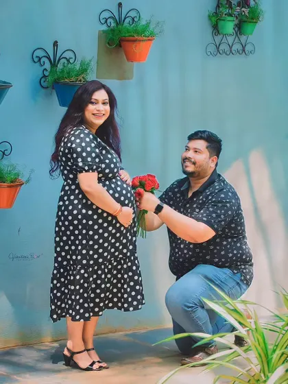 A playful and romantic moment where a partner kneels to offer a bouquet of red roses to his pregnant wife's belly.