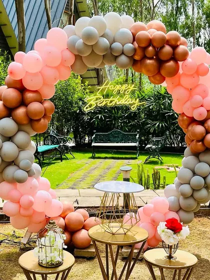 A close-up of the garden party's circular balloon arch, showing the organic arrangement of balloons and the "Happy Birthday" neon sign nestled within.