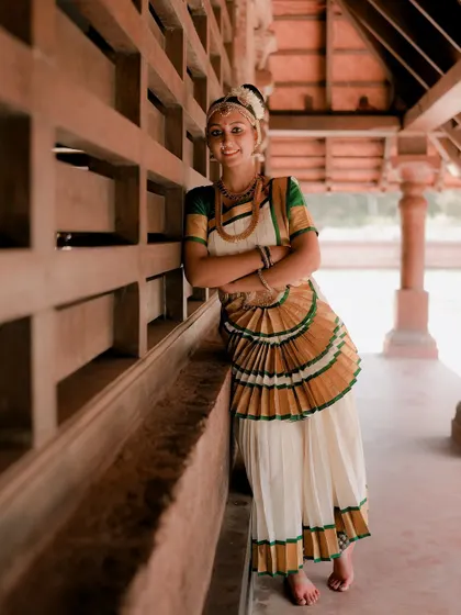 A relaxed portrait of a Mohiniyattam dancer leaning against a pillar. Her smile and casual pose offer a different, more personal glimpse of the artist.