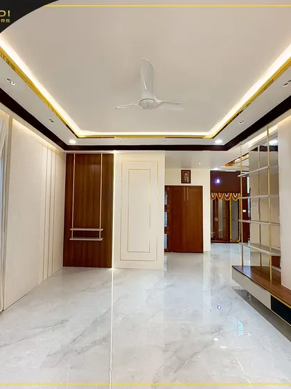 A bright and expansive hall with pristine marble flooring and a sophisticated false ceiling with cove lighting. The combination of wood paneling and light-colored walls creates a welcoming and luxurious atmosphere.