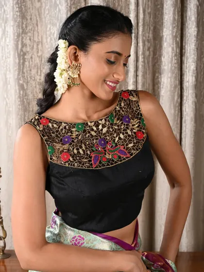 The model wears large, ornate earrings that complement the intricate embroidery on the neckline of her black blouse.