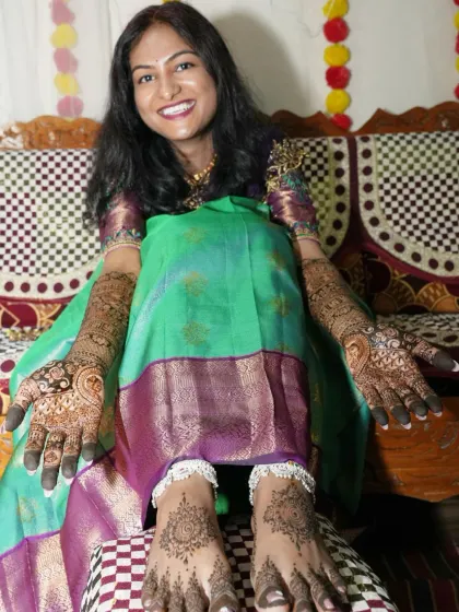 A happy bride showing her complete mehendi look, with beautiful, matching designs on her hands and feet.