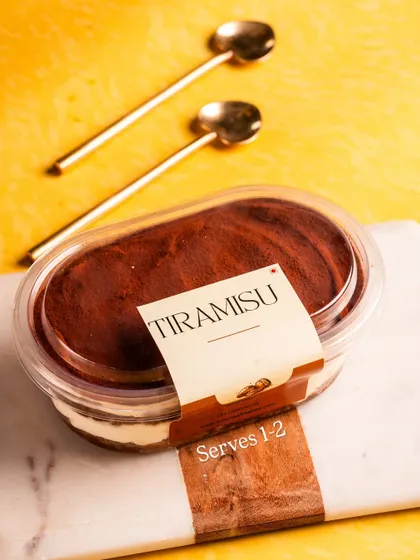 A stylish shot of our Tiramisu tub, ready to be enjoyed with two golden spoons. It's the perfect shareable personal dessert.