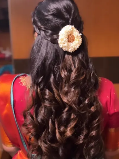 A beautiful half-up style with a braided detail and a single flower, with the rest of the hair in defined curls.