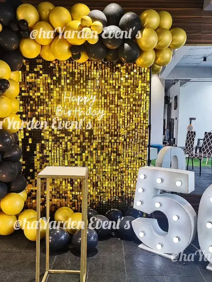 This 50th birthday setup uses large white marquee numbers for a clean, modern look against a bold black, yellow, and gold sequin background.