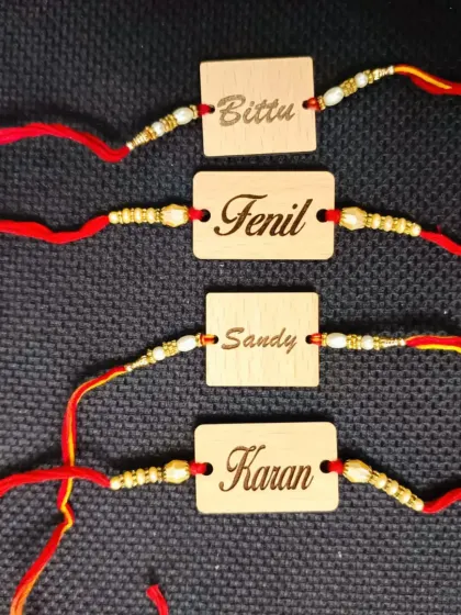 A set of four wooden name rakhis, each engraved with a different name in a clean, modern font.