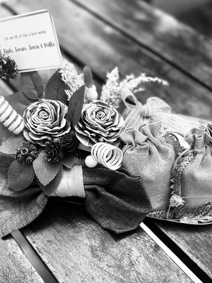 A black and white version of the gold coin platter, focusing on the rich textures of the burlap bow, wooden flowers, and delicate potli bags.