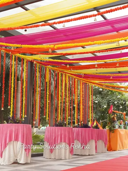 Ceiling decor can transform a space. For this Mehendi, I used vibrant drapes in yellow, pink, and orange, accented with hanging marigold garlands and bells, to create a festive canopy over the guest seating area.