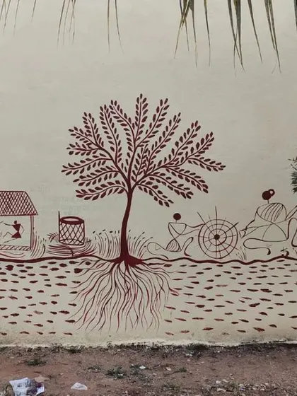 An example of a custom color palette for a Warli mural. Here, I used earthy red-brown paint on a light-colored wall to create a different feel, showing a scene of village life centered around a large tree with intricate roots.