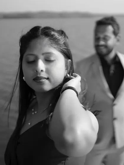 A classic black and white photo focusing on the bride-to-be with her eyes closed, while her partner stands softly out of focus in the background against a water body. This artistic shot creates a sense of calm and introspection.