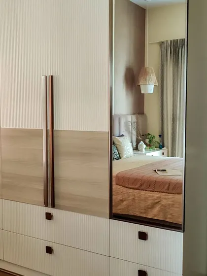 The difference is in the details. This close-up shows a custom wardrobe with a mix of fluted white and light wood grain finishes, accented by elegant rose gold handles. A full-length mirror is seamlessly integrated, reflecting the soft, serene bedroom decor.