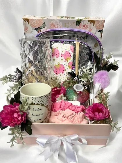 A lovely floral-themed gift box for her. This hamper includes a clear accessories pouch, a patterned mug, a crystal vase, and other pampering items, all surrounded by beautiful pink flowers.