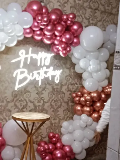 A beautiful balloon ring in metallic pink and white, set up against a wallpapered wall in what appears to be a restaurant or banquet hall space.