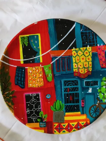 A hand-painted decorative wall plate depicting a colorful, vibrant Indian street scene. These plates are a wonderful way to bring storytelling and bright colors to your walls.