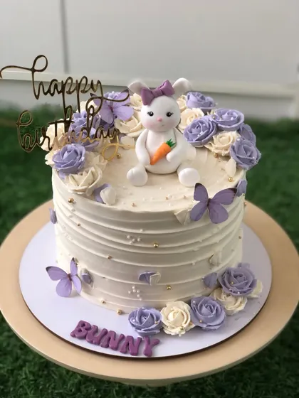 A lovely bunny-themed cake with purple and white buttercream flowers and edible butterflies.