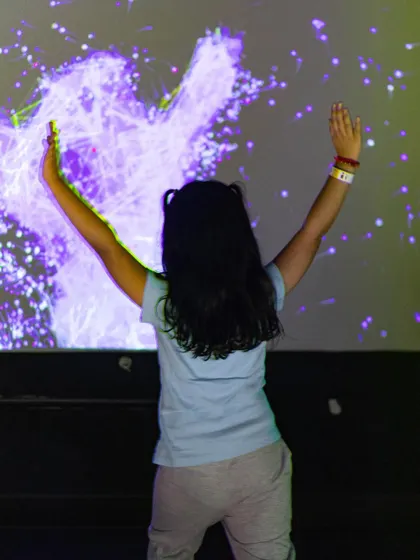 A child creates a burst of digital light on the interactive wall, feeling like she has superpowers.
