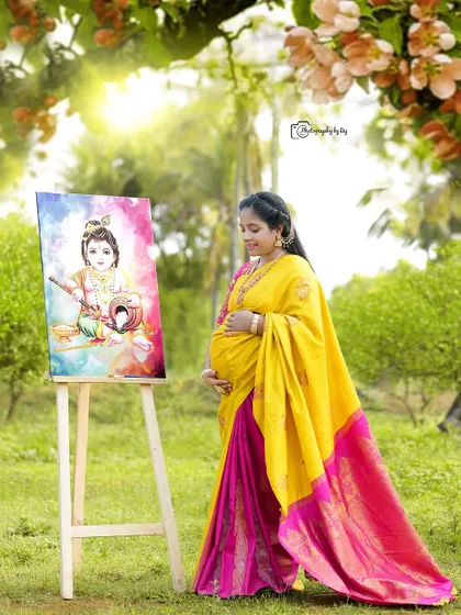 A solo maternity portrait where the mother-to-be gazes lovingly at a painting of Little Krishna. Her traditional yellow and pink saree complements the vibrant colors of the artwork, creating a harmonious and spiritual image.