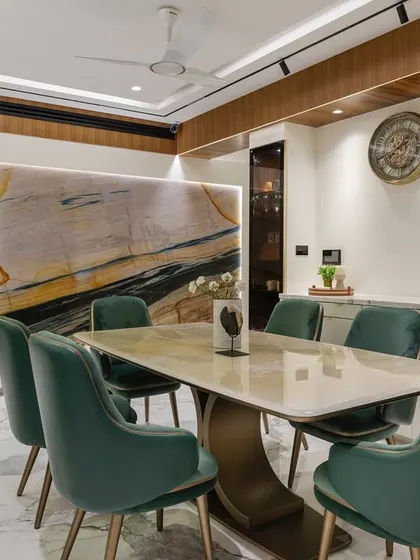 This dining room features a stunning exotic marble wall that serves as a piece of natural art. The space is completed with green velvet chairs and a sleek marble-top table.