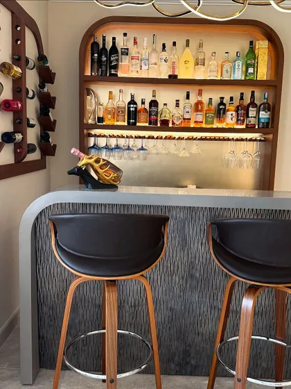 A close-up of the custom bar, highlighting the textured front panel, sleek countertop, and modern bar stools.