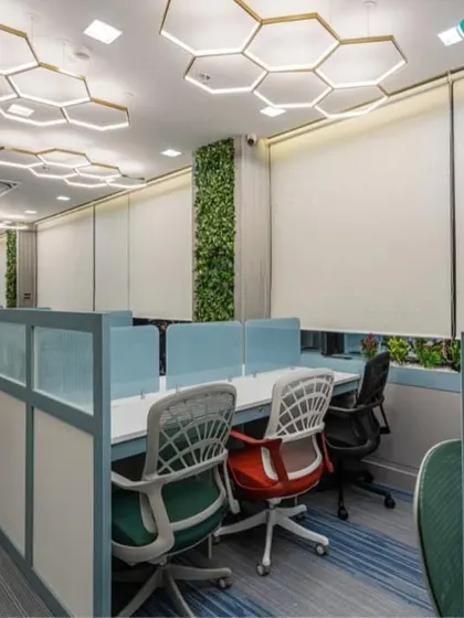 Another perspective of the open-plan office, highlighting the biophilic design with a full-height green wall and planters. The honeycomb lighting and blue-toned carpeting contribute to a calm and productive work environment.