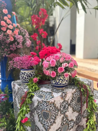 A close-up of the floral arrangements, showing the lush bouquets of pink roses and other flowers in patterned vases, with green garlands cascading down.