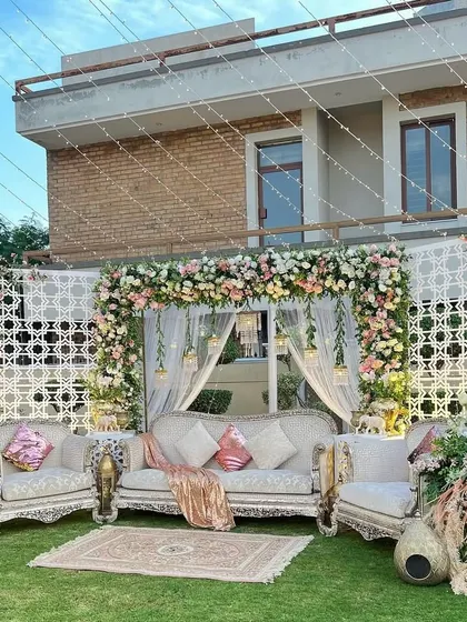 The daytime view of the elegant outdoor setup, featuring a floral arch, white lattice panels, and luxurious seating on a green lawn.